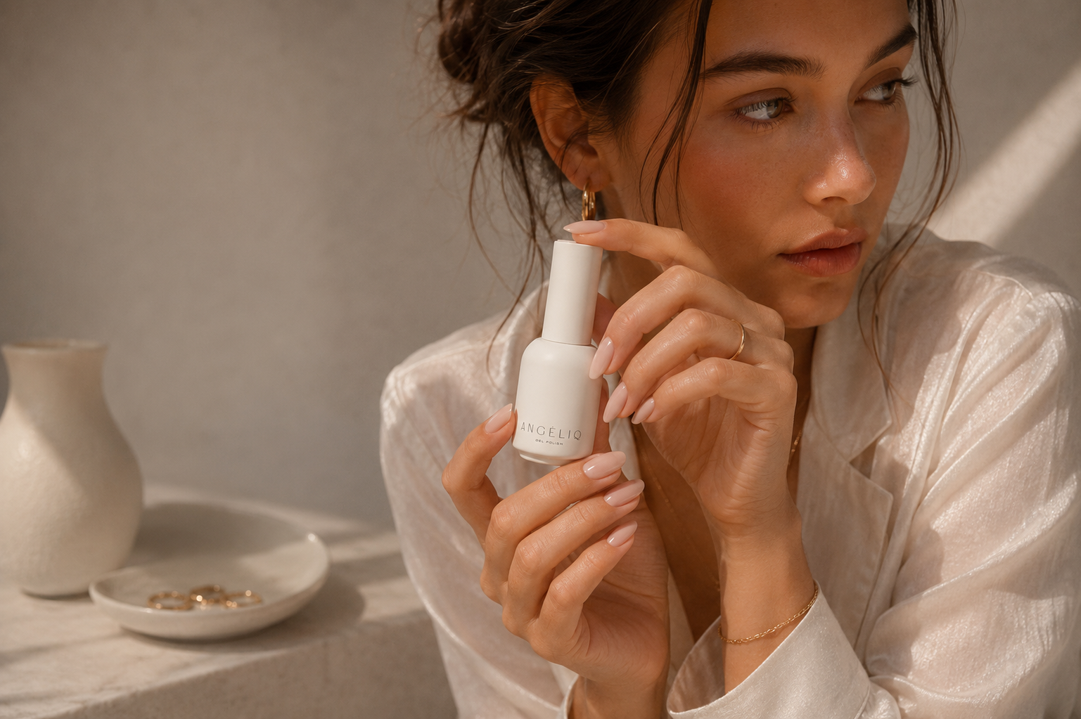 Woman holding a white nail polish bottle  branded 'Angeliq' with a neutral background